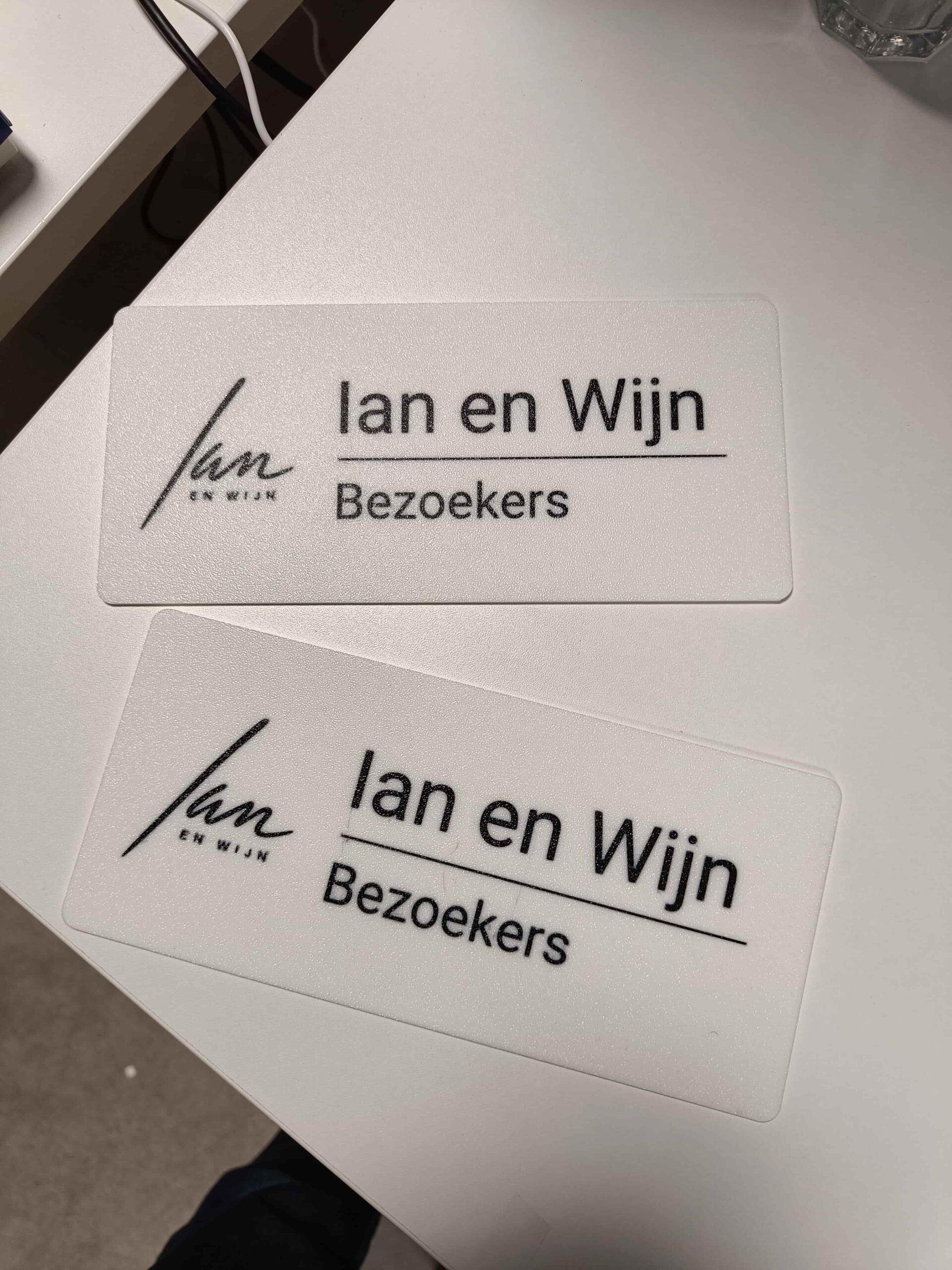 Twee witte geprinte parkeerborden met het logo van Ian en Wijn en het woord Bezoekers in zwart
